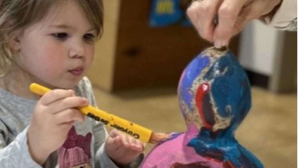 child painting a gourd birdhouse with paintbrush