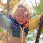 Child in bright coat climbing on tree