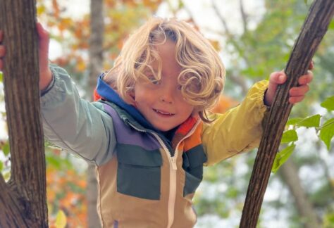 Child in bright coat climbing on tree