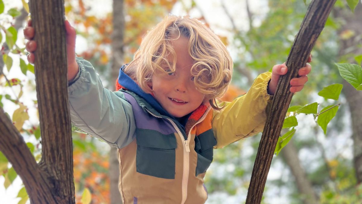 Child in bright coat climbing on tree