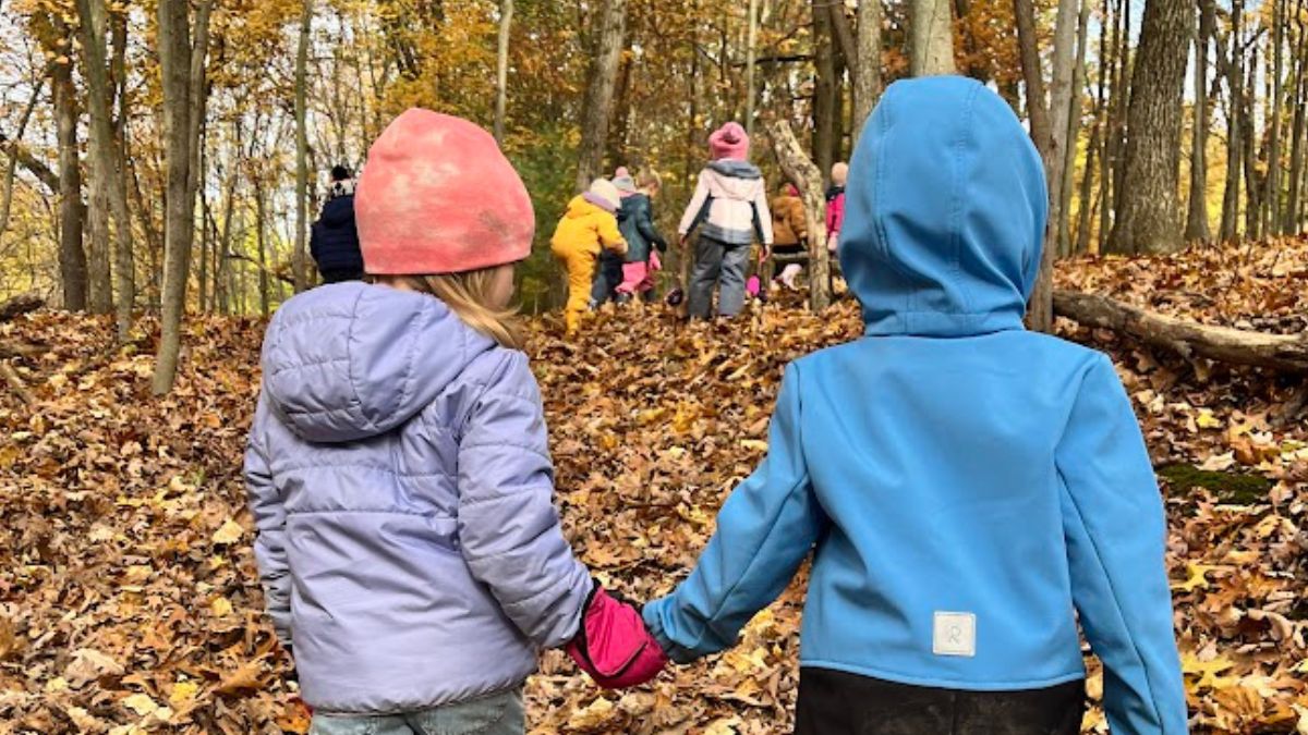 Preschoolers in fall jackets holding hands walking through woods with group