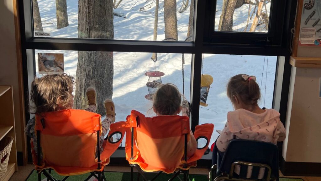 Children watching bird feeders from orange chairs indoors