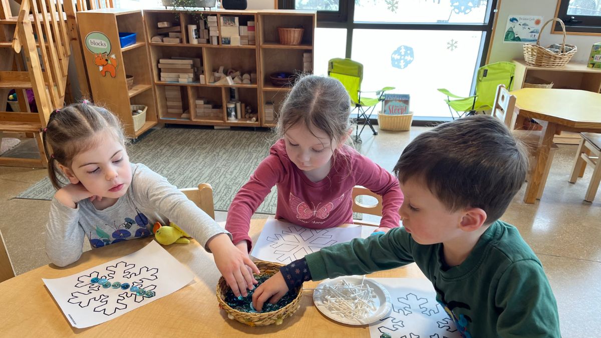 children using glass beads to make artwork at school table